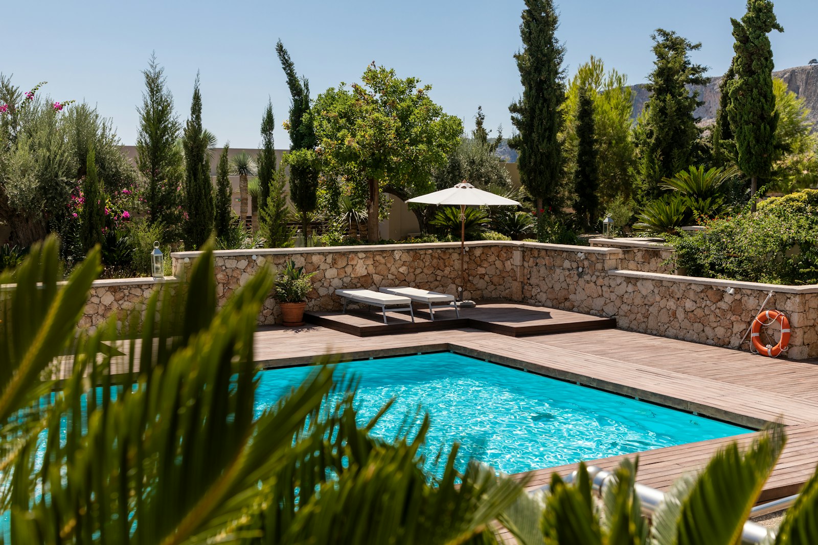 A finished backyard pool with a wood deck and stone wall